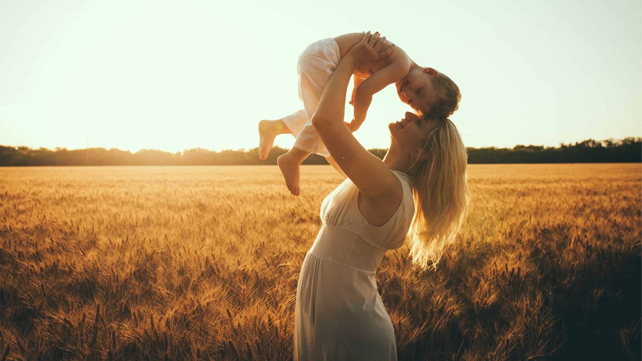 Woman standing in a field holding her child above her heard - Mom quotes for tough days