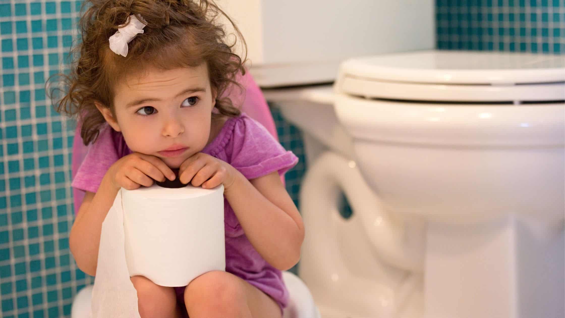 Little girl sitting in the bathroom holding a roll of toilet paper.