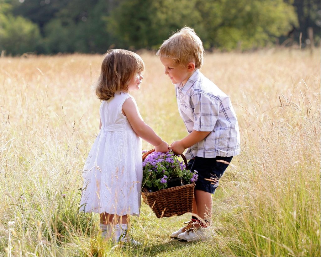 Girl and boy holding a basket of flowers in a field.