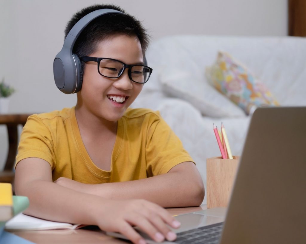 Boy doing schoolwork on his computer wearing headphones